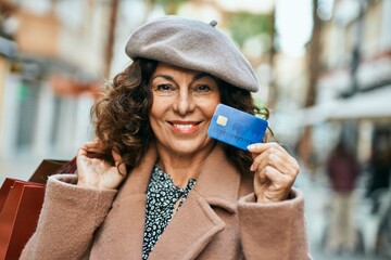 Middle age hispanic woman shopping holding credit card at the city.