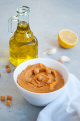 A bowl of delicious hummus with olive oil, garlic and paprika on a grey background.