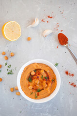 Flat lay of delicious hummus with olive oil, garlic and paprika on a grey background.