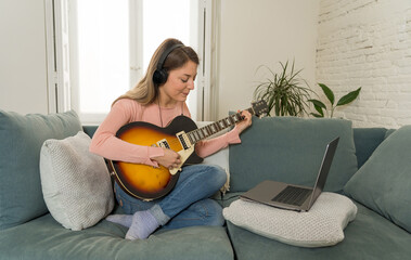 Woman playing guitar recording or streaming online video concert and lesson using laptop at home