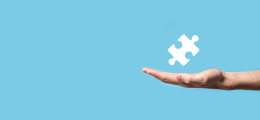 Male hand holding puzzle icon on blue background. pieces representing the merging of two companies or joint venture, partnership, Mergers and acquisition concept.