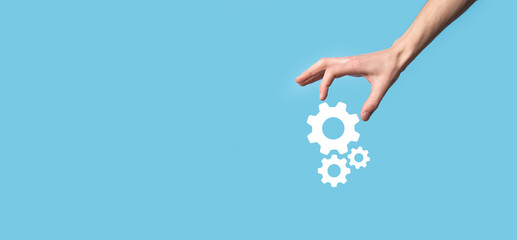 Male hand holding cog gears icon ,mechanism icon on virtual screens on blue background. Automation Software Technology Process System Business concept. Banner