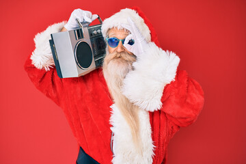 Old senior man wearing santa claus costume and boombox smiling happy doing ok sign with hand on eye looking through fingers
