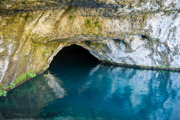 Cave in limestone rock filled blue water.