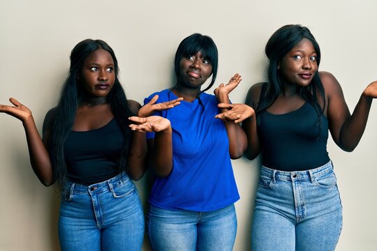 Three young african american friends wearing casual clothes clueless and confused with open arms, no idea and doubtful face.