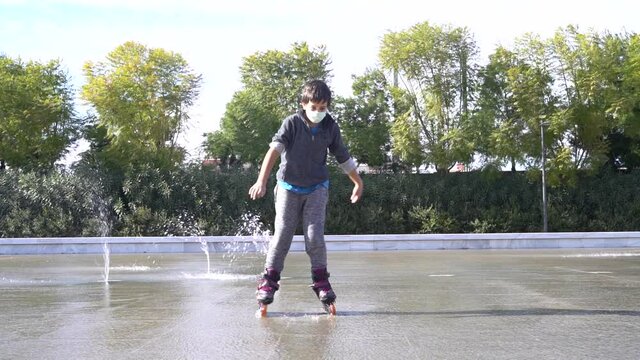Slow motion of A Caucasian boy wearing a mask and roller skates, skating in the water at the park fountain. New normal pandemic Covid 19