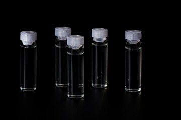 Cosmetic bottles with natural medicine, essential oil on black background. Transparent vials with hyaluronic acid.