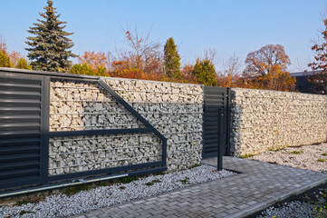 A fence made of gabions. Automatic entrance gate and wicket integrated into the wall made of a...