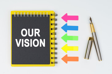 On a white background lies a pen, arrows and a notebook with the inscription - OUR VISION