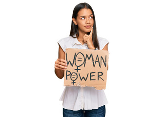 Beautiful hispanic woman holding woman power banner serious face thinking about question with hand...