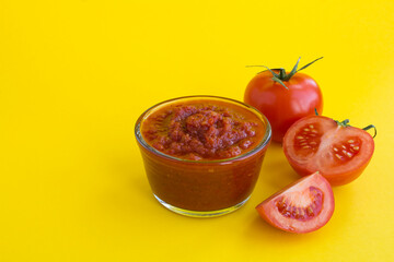 Homemade tomato ketchup in the glass bowl on the yellow background. Close-up.