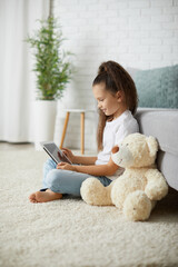 little child girl with teddy bear using digital tablet.