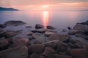 Many stones in a semicircle and mountains in the distance under a pink sunset and purple water on Baikal - 422395836