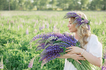 A hippy girl holding bouquet of wildflowers in her hands. Girl hid her face behind bouquet of lupins. Girl holds large bouquet of purple lupins in a flowering field. Nature concept. Present