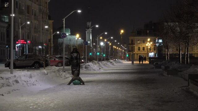 Woman carrying a child on a sled at night with winter snow in Kazan city. The mosque in background. Pedestrian street. High quality 4k footage