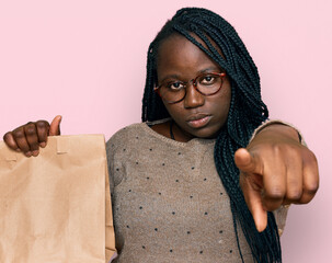 Young black woman with braids holding take away paper bag pointing with finger to the camera and to...