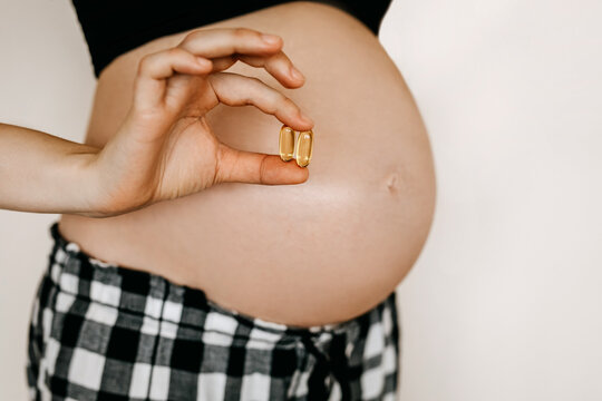 Closeup of pregnant woman holding omega 3 supplements. 