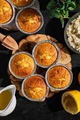 Freshly baked lemon muffins on a black wooden table. Homemade delicious magdalena, proofing after baking, ingredients on the table nearby, top view with copy space
