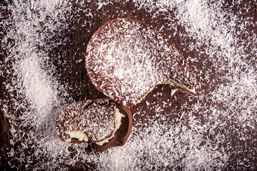 Top view of a cracked chocolate easter egg with coconut filling and grated coconut on the top on a wooden table.