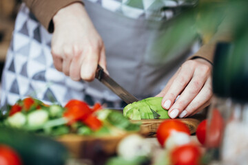 Woman cutting an avocado for salad on wooden board. Close up view.