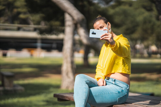 Beautiful Caucasian woman in a yellow crop jacket and face mask taking selin the park