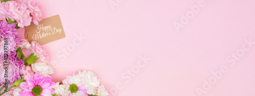 Happy Mothers Day gift tag with corner border of pink and white flowers. Overhead view on a pink banner background. Copy space.