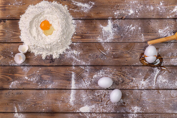 Chicken eggs, a pile of wheat flour and a rolling pin on a brown board background