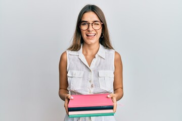 Young hispanic woman holding books winking looking at the camera with sexy expression, cheerful and...