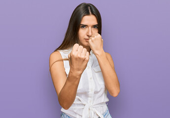 Young hispanic woman wearing casual clothes ready to fight with fist defense gesture, angry and...