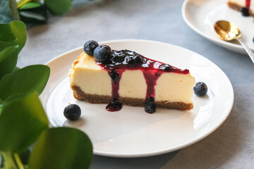 Portion of classic cheesecake poured blueberry jam. Slice of delicious cake with fresh berries on plate. Summer sweet dessert.