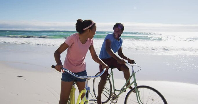 African american couple smiling and riding bikes on the beach
