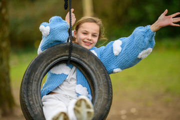Girl Waving on a Tyre Swing. A young girl waving and smiling while swinging on a black tyre swing at a park.