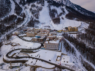 Winter aerial view of the road to ski resort Krasnaya Polyana with apartment buildings, hotels, restaurants and ski lifts. Beautiful winter landscape from drone.