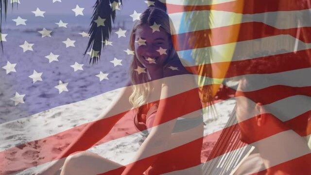 Animation of american flag waving over couple in deckchairs laughing on beach