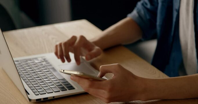 Midsection of man texting on smartphone and using laptop at desk
