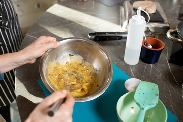 Hands of mature female mixing raw ingredients for stew with whisker in metallic bowl while cooking by kitchen table at master class