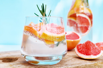 Summer cocktail with grapefruit and rosemary and juicy slices citrus fruits. Fresh healthy grapefruit beverage on sunlight with shadows. Creative drink on blue pastel background.