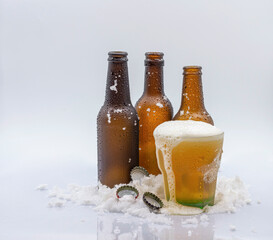 THREE EMPTY COLD BEER BOTTLES AND ONE COLD BEER GLASS WITH BEER AND LOTS OF FOAM