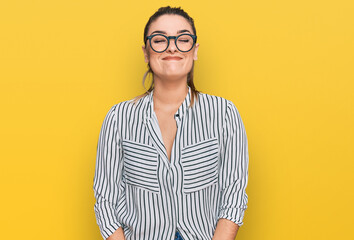 Young caucasian woman wearing business shirt and glasses puffing cheeks with funny face. mouth inflated with air, crazy expression.
