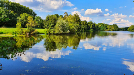 Fototapeta na wymiar River with cloud reflections and spring green trees.