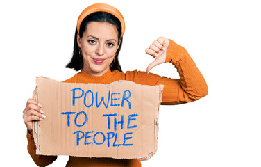 Young hispanic girl holding power to the people banner with angry face, negative sign showing...