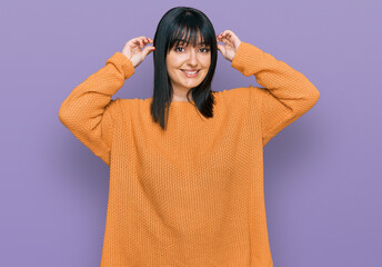 Young hispanic woman wearing casual clothes smiling pulling ears with fingers, funny gesture....