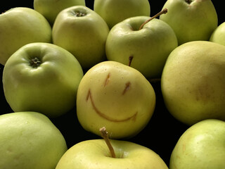 Green apples with a picture of a smile. Ripe fruits isolated on black. Apples with face pattern. Concept: joy, happiness, positive.