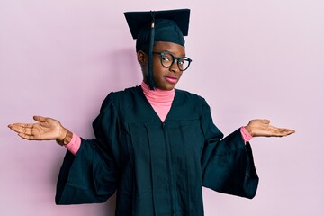 Young african american girl wearing graduation cap and ceremony robe clueless and confused...