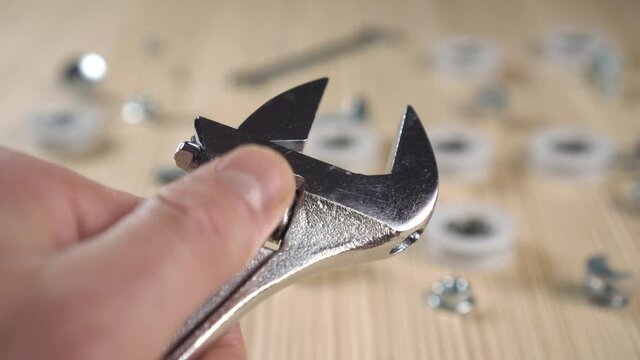 Close-up adjustment of steel monkey wrench against background of repair parts in blur on wooden work table