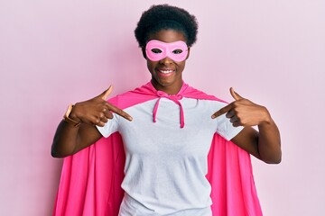 Young african american girl wearing superhero mask and cape costume looking confident with smile on...