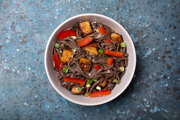 A dish of Asian cuisine. Soba noodles with red bell pepper, green onions and fried tofu cheese