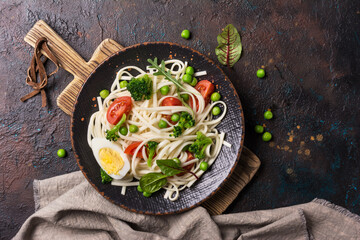 A dish of Asian cuisine. Udon noodles with cherry tomatoes, broccoli and green pea