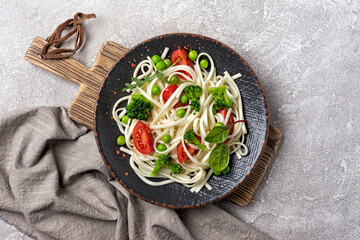 A dish of Asian cuisine. Udon noodles with cherry tomatoes, broccoli and green pea