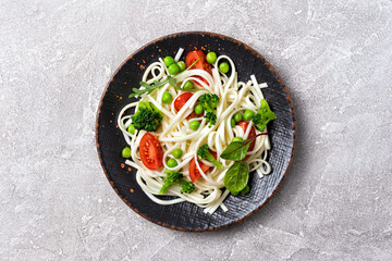 A dish of Asian cuisine. Udon noodles with cherry tomatoes, broccoli and green pea